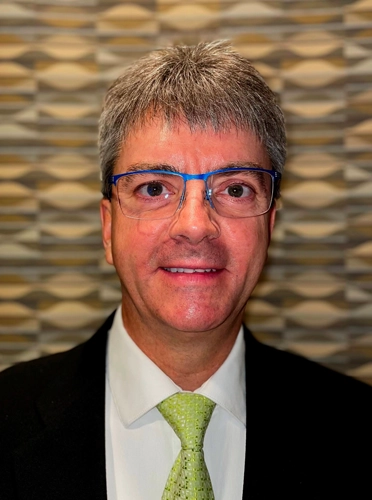 Brian Norman smiling in blue glasses and a green tie.