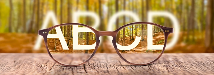 Eye Doctor Cape Girardeau MO First Exam A pair of glasses sitting on a wooden table. ABCD listed in the background.