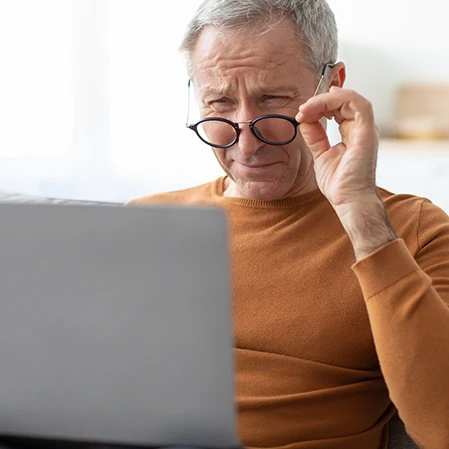 A man wearing glasses while looking at a laptop.